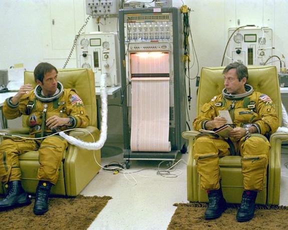 STS-1 astronauts Robert Crippen (left) and John Young (right) discuss checklist items during suit-up in the Operations and Checkout Building prior to departure for the launch pad during the final countdown rehearsal before launch.
