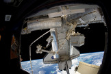 Discovery STS-133 astronaut Steve Bowen stands at the tip of the International Space Station's Canadian robotic arm, with the Earth and space shuttle in the background, during the second spacewalk of his mission on March 2, 2011.