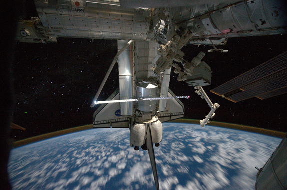 This view of the space shuttle Atlantis while still docked with the International Space Station was taken by a crew member aboard the station on the final day of joint activities between the crew members for the STS-135 and Expedition 28 missions. The robotic arm on the shuttle appears to be saluting "good-bye" to the station. Earth's airglow is seen as a thin blue line above Earth's horizon. The Raffaello multi-purpose logistics module, full of items to be returned to Earth, is seen in the aft cargo bay, July 19. 2011. Flight Day 12.