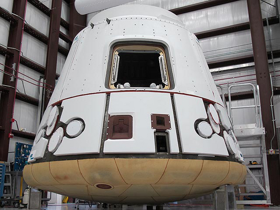 In the SpaceX hangar at Cape Canaveral, the Dragon spacecraft prepares for integration with the Falcon 9 launch vehicle. Visible at the base of the spacecraft is Dragon’s heat shield, made of PICA-X, the SpaceX manufactured variation on NASA’s Phenolic Impregnated Carbon Ablator (PICA) heat shield material. Dragon will reenter the Earth’s atmosphere at around 7 kilometers per second (15,660 miles per hour), heating the exterior up to 1850 degrees Celsius. However, just a few inches of the PICA-X material will keep the interior of the spacecraft at a comfortable temperature.