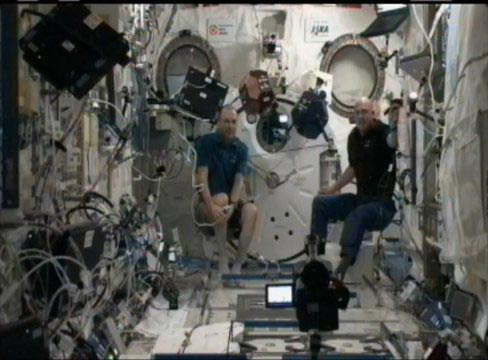Astronauts Don Pettit (left) and André Kuipers (right) watch as two SPHERES robots perform their operations as part of the SPHERES Zero-Robotics tournament.