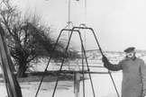 Dr. Robert H. Goddard and a liquid oxygen-gasoline rocket in the frame from which it was fired on March 16, 1926, at Auburn, Mass. The rocket flew to a height of 41 feet and returned to Earth in two and a half seconds.
