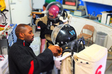 Packing for the Mars Desert Research Station is a lot like preparing for a camping trip, except for the equipment for science experiments. In this picture, taken during a previous MDRS mission, Habib Palenfo assists Paula Crock and John Reynolds (background) with putting on spacesuits.