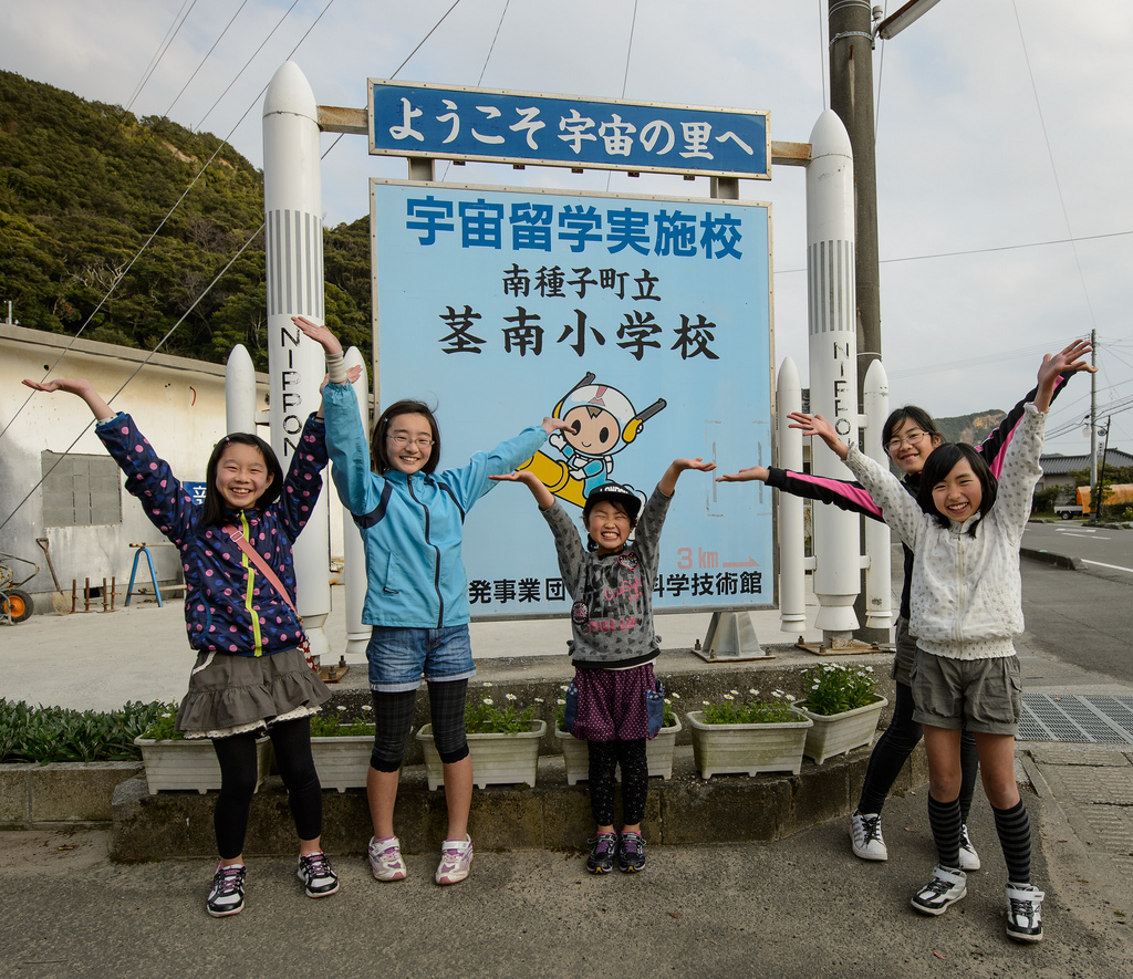 School Girls Pose in Front of Sign Featuring Mascot ‘Chuta-Kun’
