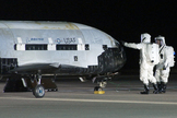 An X-37B robotic space plane sits on the Vandenberg Air Force base runway during post-landing operations on Dec. 3, 2010. Personnel in self-contained protective atmospheric suits conduct initial checks on the robot space vehicle after its landing.