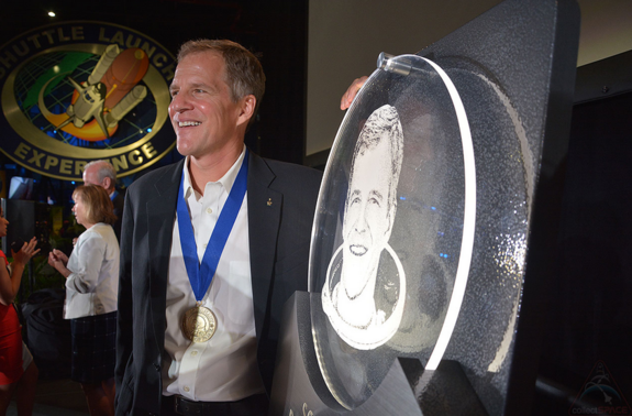 Scott Parazynski poses next to his U.S. Astronaut Hall of Fame plaque. The display features his portrait and space shuttle mission patches.