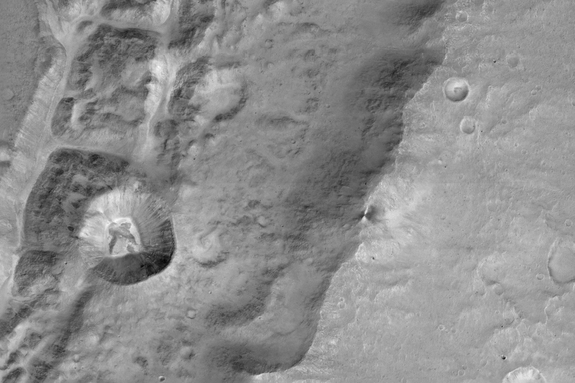 Image of a 0.9 mile-size (1.4 kilometers) crater (left-center) _n the rim of a larger crater near the Mars equator. It was acquired at 7.2 meters/pixel by the Colour and Stereo Surface Imaging System (CaSSIS) aboard the European Space Agency's ExoMars Trace Gas Orbiter. 