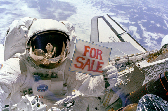 Astronaut Dale Gardner holds up a "For Sale" sign, referring to the two satellites, Palapa B-2 and Westar 6, that they retrieved from orbit. Astronaut Joseph Allen IV is reflected in Gardner